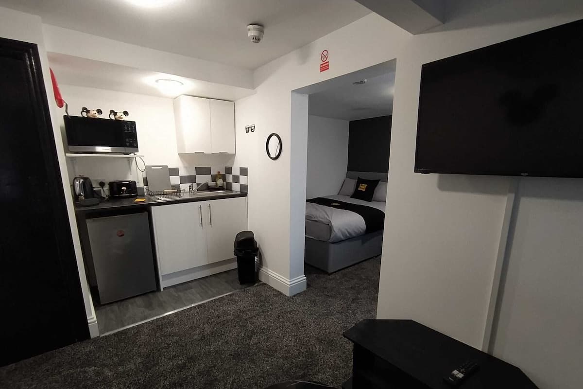 Ein kompaktes Hotelzimmer mit Küchenzeile, einem Bett, einem Fernseher und einer kleinen Sitzecke.