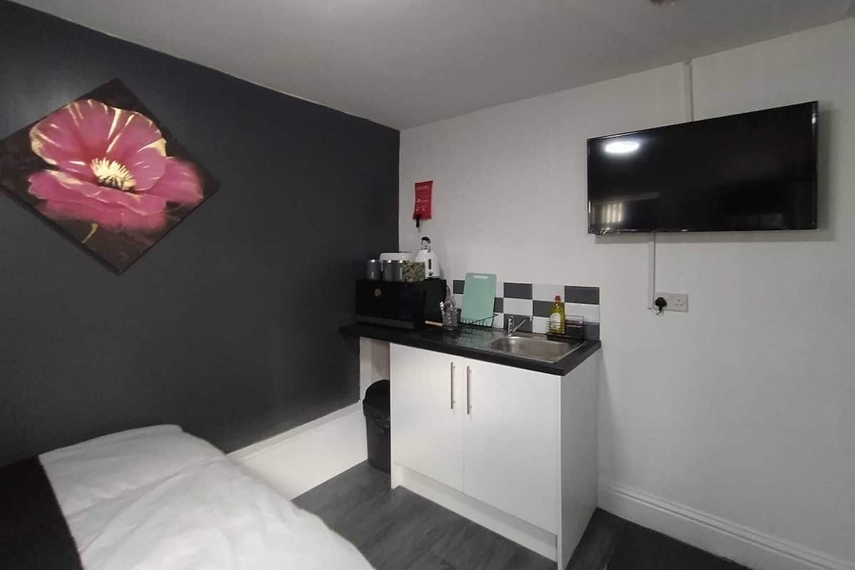 Ein kompaktes Zimmer mit Bett, einer kleinen Küchenzeile, einem an der Wand montierten Fernseher und einem dekorativen Blumenbild.