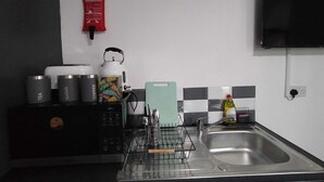 Eine Küche mit Mikrowelle, Kaffeemaschine, Zucker und Tee, einem Wasserkocher, Schneidebrett und Spüle.