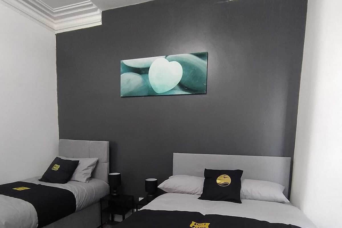 Ein Hotelzimmer mit zwei Betten, jeweils mit einer schwarz-weißen Tagesdecke, einem Kopfteil und einem Kopfkissen mit einem Logo. Darüber an der Wand hängt ein Gemälde.
