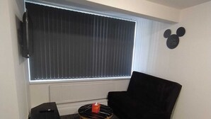 Ein Zimmer mit einem schwarzen Ledersessel, einem kleinen runden Tisch mit goldener Basis, einem schwarzen Lautsprecher und einer Wanddekoration mit Mickey Mouse.