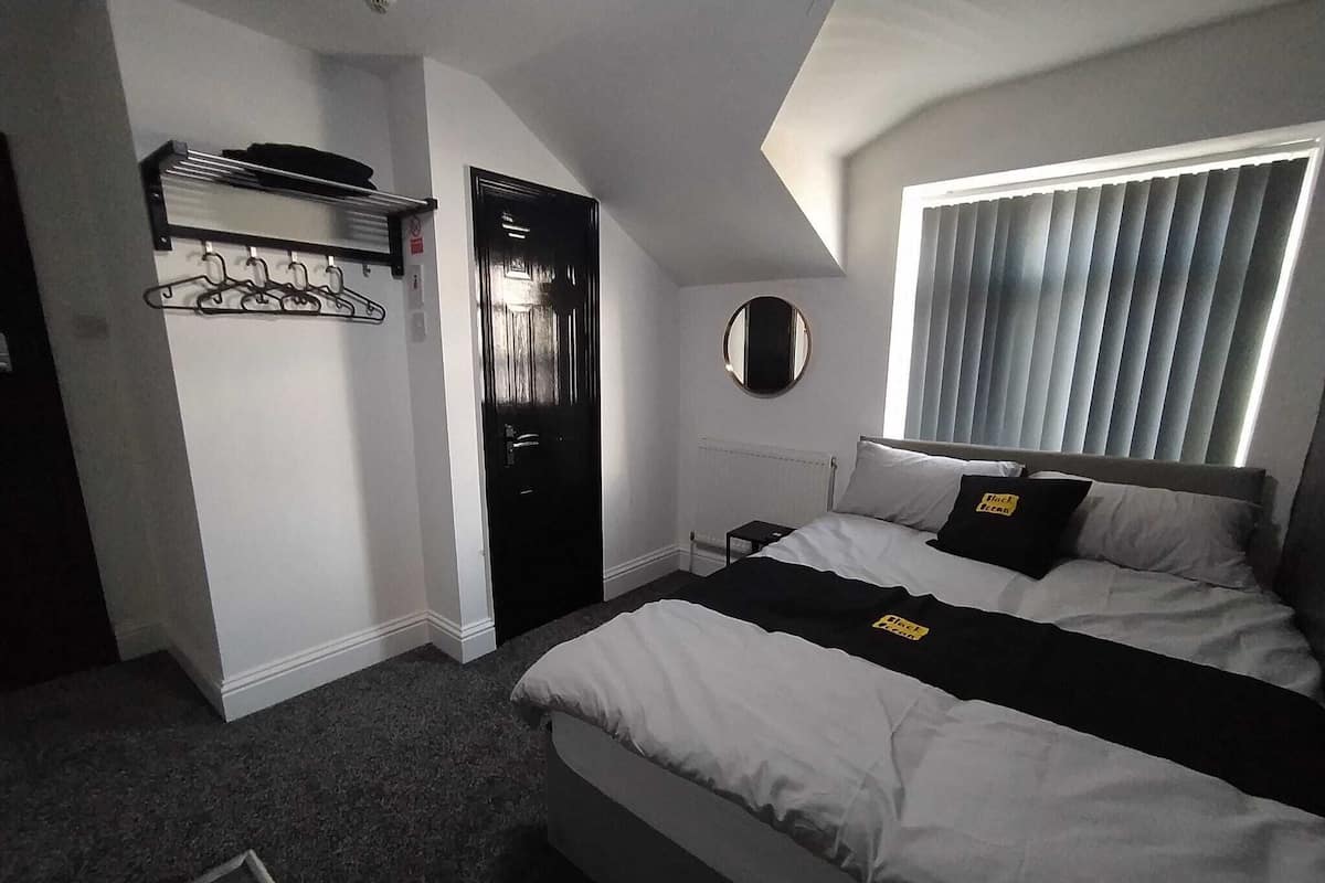 Ein Hotelzimmer mit einem Bett, einem Kleiderhaken, einer Tür und einem Fenster mit Jalousien.