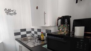 Eine kompakte Küche mit Spüle, Mikrowelle und Kaffeemaschine. An der Wand hängt eine Feuerdecke und ein Schild mit der Aufschrift 'Coffee Time'.