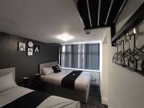 Une chambre d’hôtel avec deux lits, une fenêtre avec des stores, une horloge et des tableaux encadrés au mur.