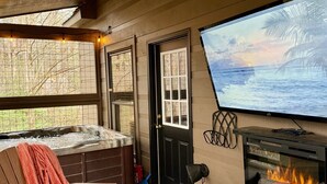 A cozy room with a hot tub, a fireplace, a TV, and a view of the ocean. - Private Deck with Hot Tub & Outdoor TV, Fun Game Loft, Fast Starlink Internet ⭐️ (Sevierville)