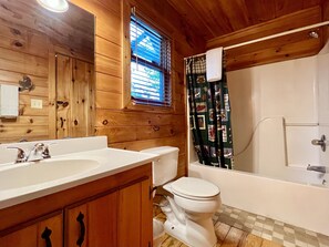 Une salle de bain rustique, aménagée dans une cabane en bois, avec un lavabo, des toilettes et une baignoire.