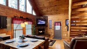 A cozy cabin interior with a wooden dining table, leather sofas, a fireplace, and a television. - Private Deck with Hot Tub & Outdoor TV, Fun Game Loft, Fast Starlink Internet ⭐️ (Sevierville)
