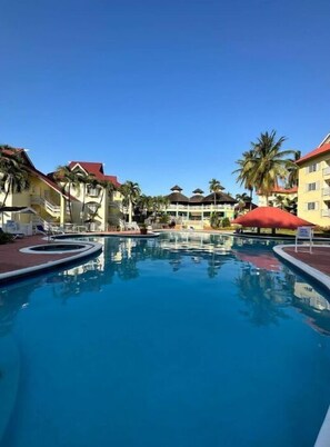 A swimming pool with lounge chairs and palm trees, surrounded by buildings with red roofs. - Bucket List Stays (Ocho Rios)