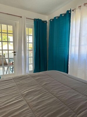 A bedroom with a bed, a window with curtains, and a door. - Bucket List Stays (Ocho Rios)