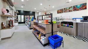 A clean, well-organized grocery store with shelves stocked with various products, a blue shopping basket, and a refrigerator in the background.