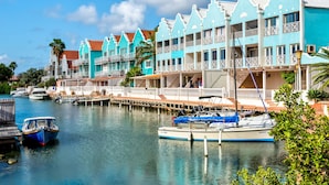 Un hotel frente al agua con varios balcones, un muelle con barcos y un cielo azul despejado.