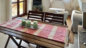 A dining area with a table set for two, a television on a stand, and a sofa in the background.