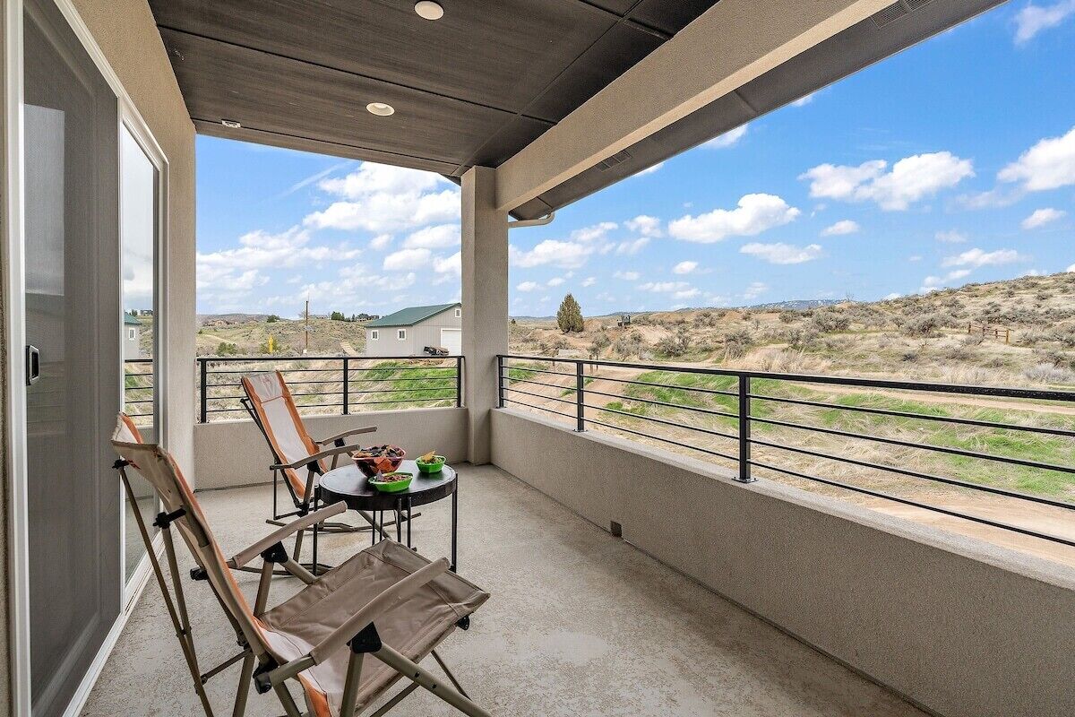 A balcony with a table and chairs, a view of a hilly landscape, and a clear sky.