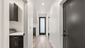 Ein schmaler Korridor mit Holzboden, einer schwarzen Tür rechts und einer weißen Wand mit einem schwarzen Schrank links.