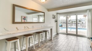 Un baño moderno con encimera de mármol, cuatro taburetes, un espejo grande y vistas a una piscina a través de puertas de cristal.