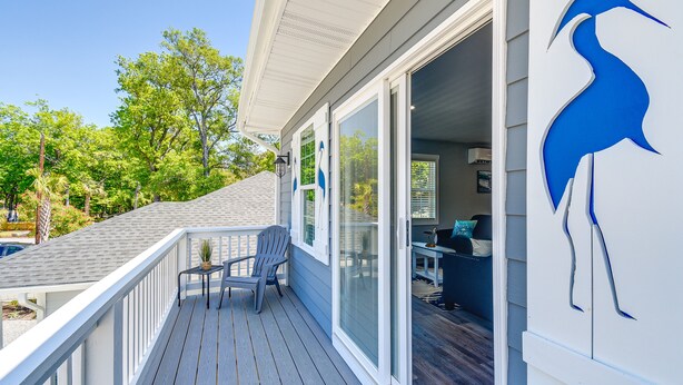 A deck with a chair and a small table, a sliding glass door, and a bird sculpture on the wall.