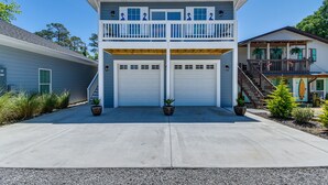 A two-story house with a balcony, two garage doors, and a staircase leading to a porch.