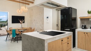 Une cuisine moderne dotée d’un îlot central, de meubles en bois, d’un réfrigérateur noir et de luminaires suspendus.