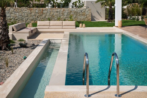 A swimming pool with a stone wall and a beige sofa. - New-build Villa Riza Chania private pool and Roofgarden with jacuzzi (Chania)