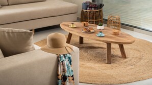 Un salon avec un canapé beige, une table basse en bois surmontée d’un tapis tissé et des paniers en osier.
