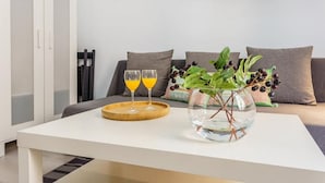 Uma sala de estar moderna com uma mesa de centro branca, um vaso de vidro com plantas verdes e dois copos de suco de laranja.