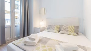 Quarto de hotel com uma cama grande, mesa de cabeceira, espelho e janela com cortinas.