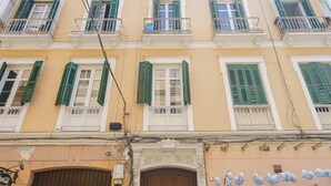 Um edifício com várias janelas, algumas com persianas verdes, e uma fachada visível com uma placa que diz 