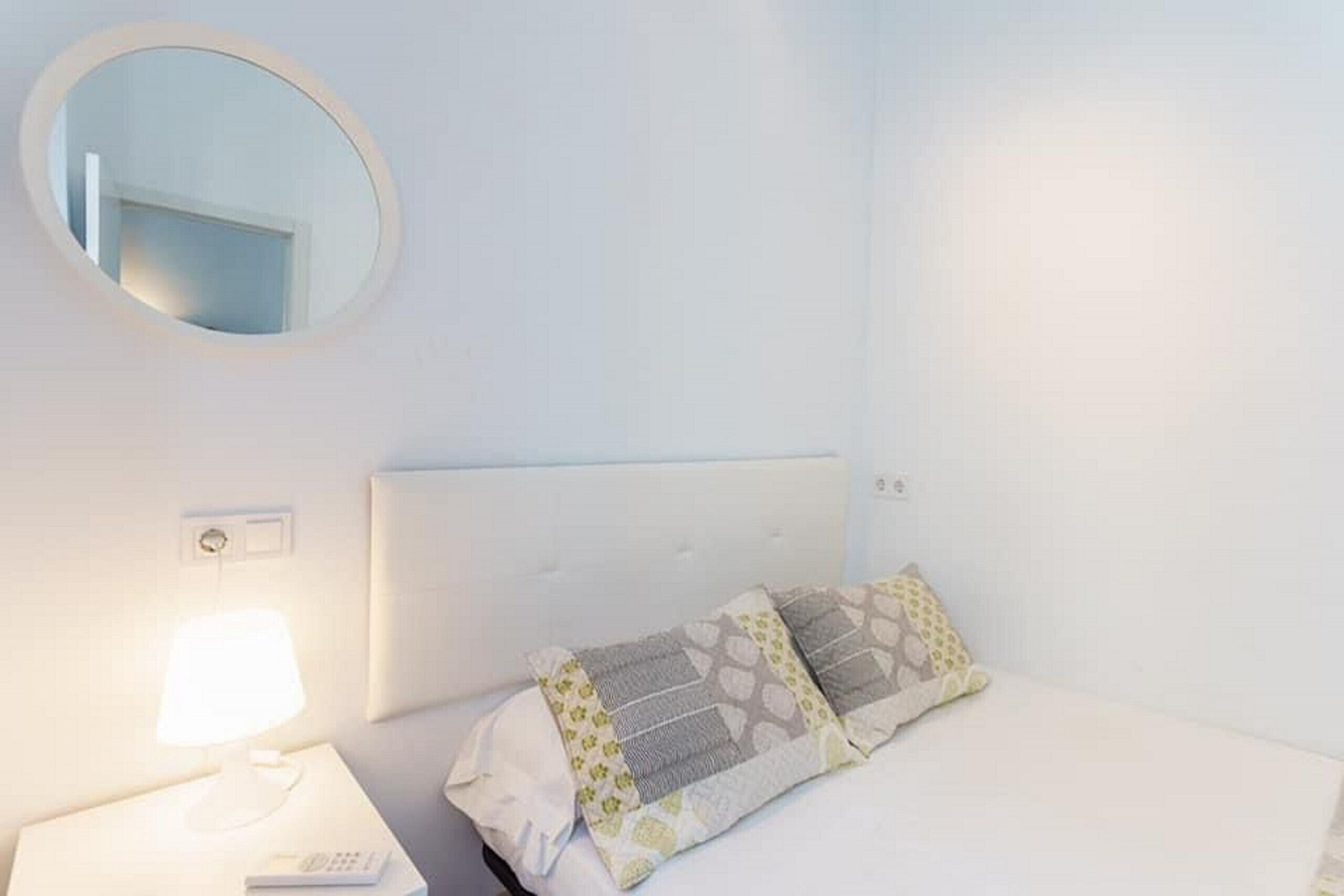 Une chambre avec un lit simple, un miroir rond et une table de chevet avec une lampe.