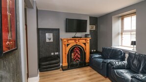 A modern living room with a fireplace, leather sofa, and a flat-screen TV mounted on the wall. - 78 King Street (Wexford)