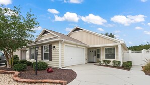 Ein eingeschossiges Haus mit Garage, überdachter Veranda und kleinem Vorgarten mit Baum und Sträuchern.