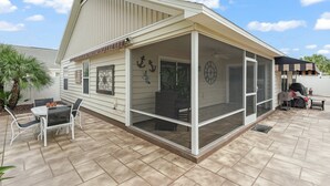 Eine überdachte Terrasse mit Tisch, Stühlen, einem Grill und einer Zierwand.