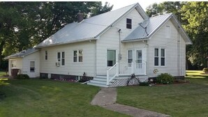 A single-story white house with a front porch, a small front yard, and a metal roof.