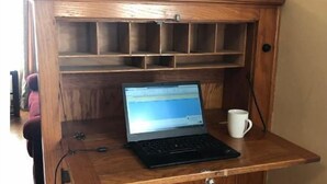 A wooden desk with a laptop and a mug, featuring a built-in shelf and a cabinet.