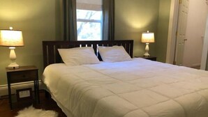 A neatly made bed with white bedding, two bedside lamps, and a fluffy white rug on a wooden floor.