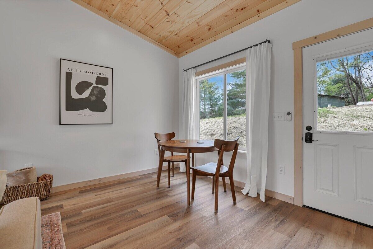 Une pièce avec un plafond en bois, une table à manger avec des chaises, une œuvre d’art encadrée au mur et une porte donnant sur l’extérieur.