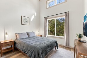 A bedroom with a large bed, two bedside tables with lamps, a window with curtains, and a painting on the wall. - Onyx - Near Hocking Hills (Rockbridge)