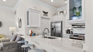 A modern kitchen with white cabinetry, a stainless steel refrigerator, an oven, and a countertop with stools. - 4BR Spacious Beach Home with Private Pool+ Studio Apartment | Southern Nights (Destin)