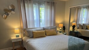 Een slaapkamer met een groot bed, twee nachtkastjes, een wandspiegel en een raam met gordijnen.