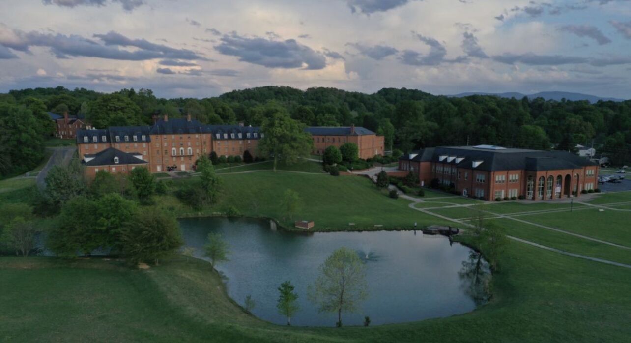 A large brick building with multiple wings, a central courtyard, and a small pond.