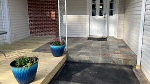 Een overdekte veranda met twee grote plantenbakken, een bakstenen muur en een witte deur met ruitpanelen.