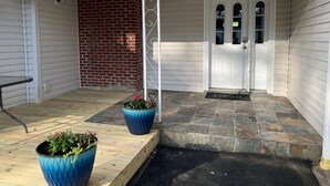 Een overdekte veranda met een witte deur, een bakstenen muur en twee grote blauwe plantenbakken.