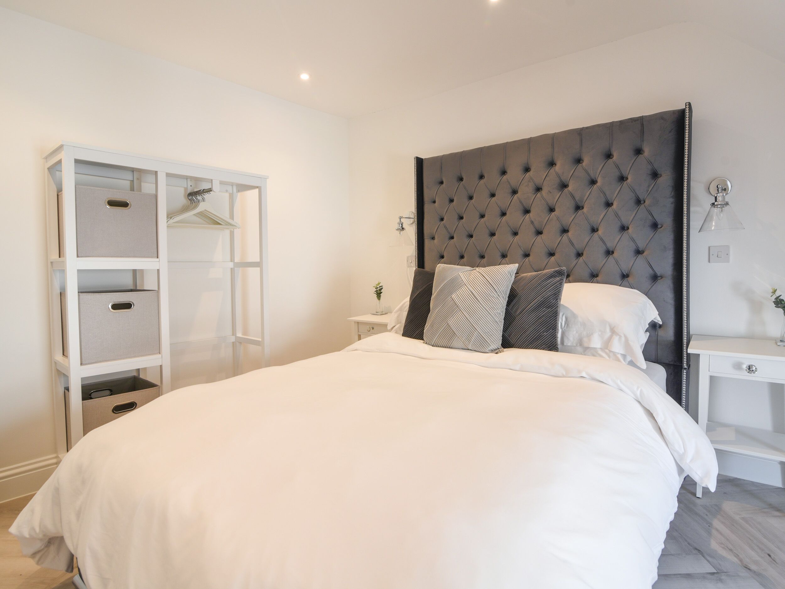Un dormitorio con una cama grande, un armario con varios estantes, una mesita de noche y un cabecero moderno.