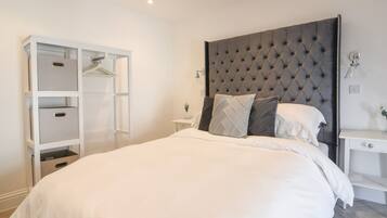 Un dormitorio con una cama grande, un armario con varios estantes, una mesita de noche y un cabecero moderno.