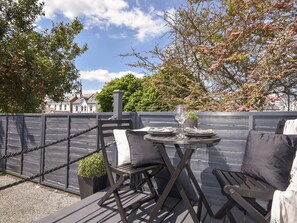 An outdoor seating area with a table set for two, a potted plant, and a view of a building in the background. - Fore Street House - Apartment 2 (Seaton)