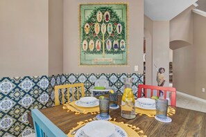 A dining area with a table set for four, a decorative wall piece, patterned tiles, and a staircase in the background.