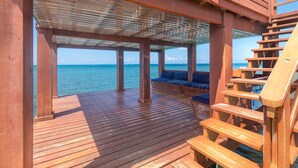 Une terrasse en bois dotée d’un espace salon couvert et d’un escalier menant à un niveau supérieur.