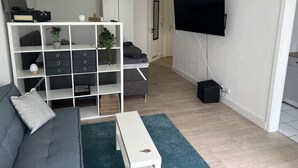 A modern living room with a grey sofa, a white coffee table, a TV mounted on the wall, and a white shelving unit with decorative items. - Wunderschöne 1-zimmer Wohnung (Wiesbaden)