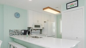 A kitchen with white cabinets, a microwave, a refrigerator, a sink, and a clock on the wall. - Top floor ocean front condo in Ocean Dunes! (Kure Beach)