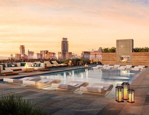 A rooftop pool with lounge chairs and a fire feature, overlooking a cityscape at sunset. - 2BD Condo-Rainey St-Best views-RT Pool (Austin)