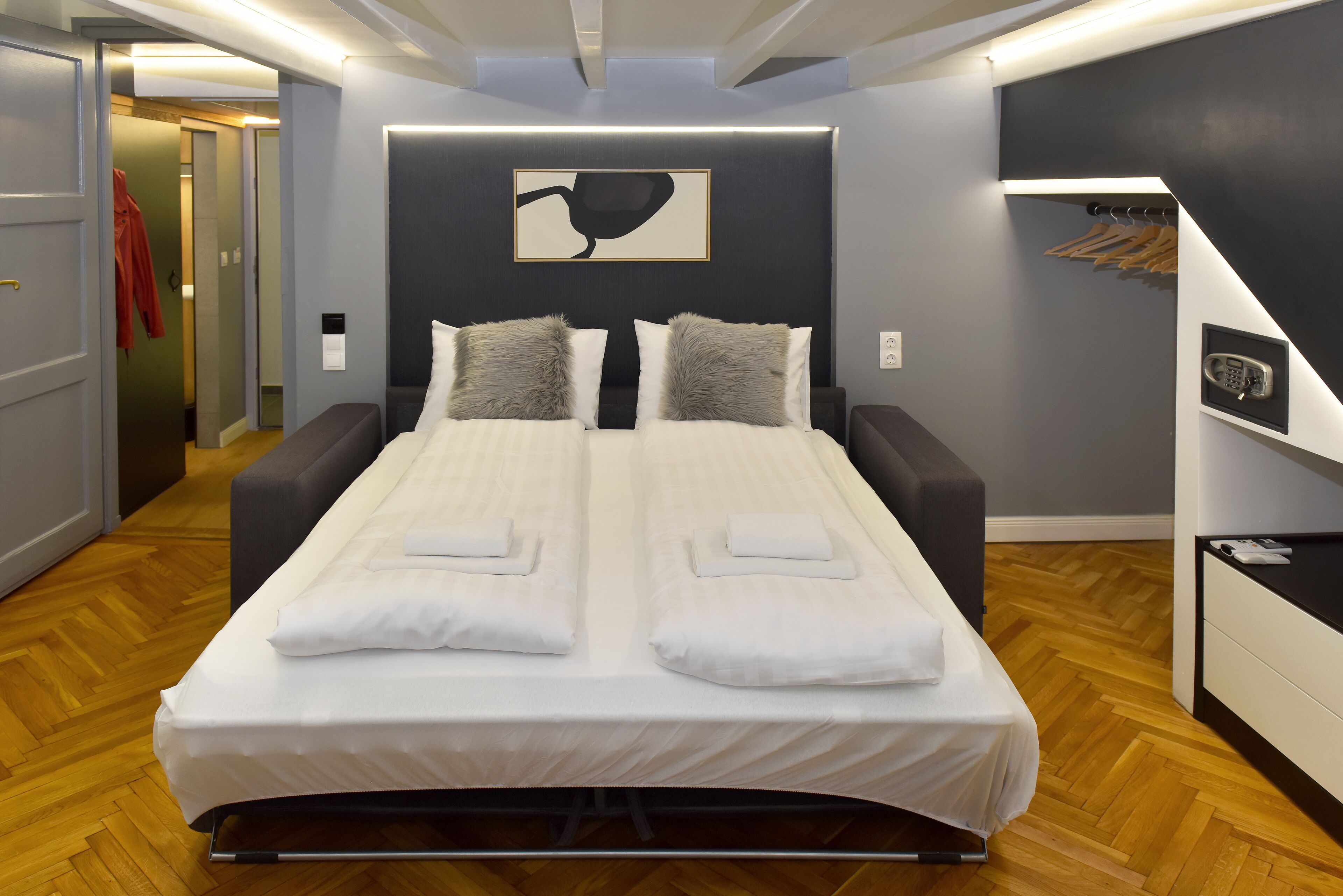 A modern bedroom with a large bed, a bedside table, a built-in wardrobe, and a coat rack.